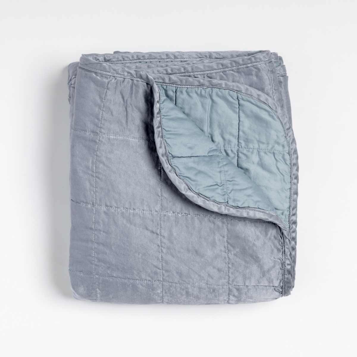 Sel Blanket | Tahoe Blue | an overhead shot of a quilted charmeuse blanket in tahoe blue, a crisp true blue, with a corner folded down, showing its cotton sateen back.