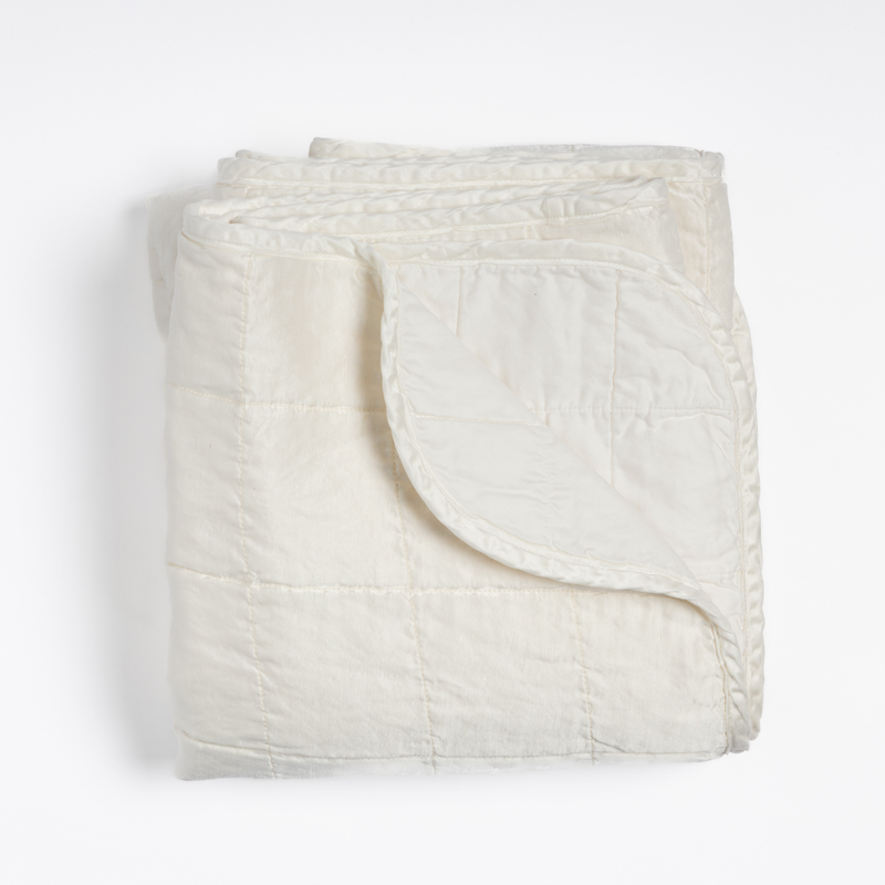 Sel Blanket | Winter White | an overhead shot of a quilted charmeuse blanket in winter white, a softer and warmer tone than our classic white, with a corner folded down, showing its cotton sateen back.