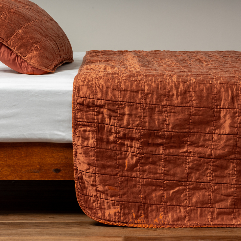 Sel Coverlet | Autumn | A side shot of a square quilted charmeuse coverlet in autumn, a rich terracotta tone, with its matching sham.