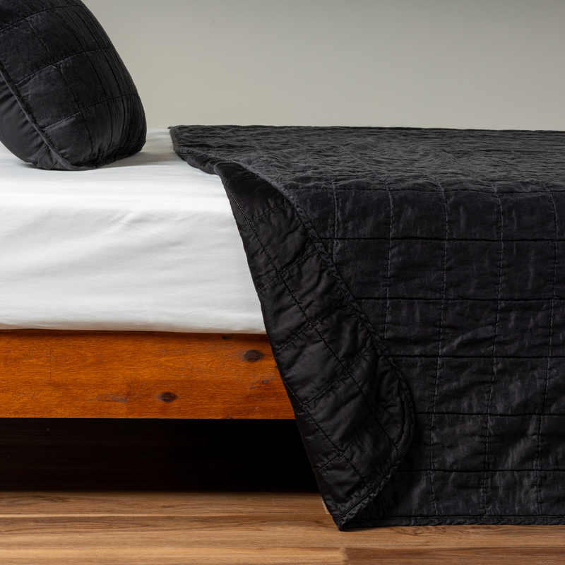 Sel Coverlet | Corvino | A side shot of a square quilted charmeuse coverlet with its matching sham in corvino, our classic black, the corner of the coverlet peeled back, revealing the cotton sateen back.