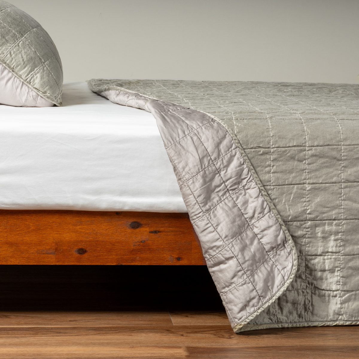 Sel Coverlet | Fog | A side shot of a square quilted charmeuse coverlet in fog, a soft mid-tone grey, with its matching sham, the corner of the coverlet peeled back, revealing the cotton sateen back.