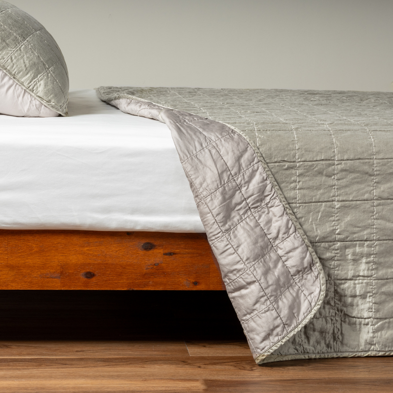 Sel Coverlet | Fog | A side shot of a square quilted charmeuse coverlet in fog, a soft mid-tone grey, with its matching sham, the corner of the coverlet peeled back, revealing the cotton sateen back.