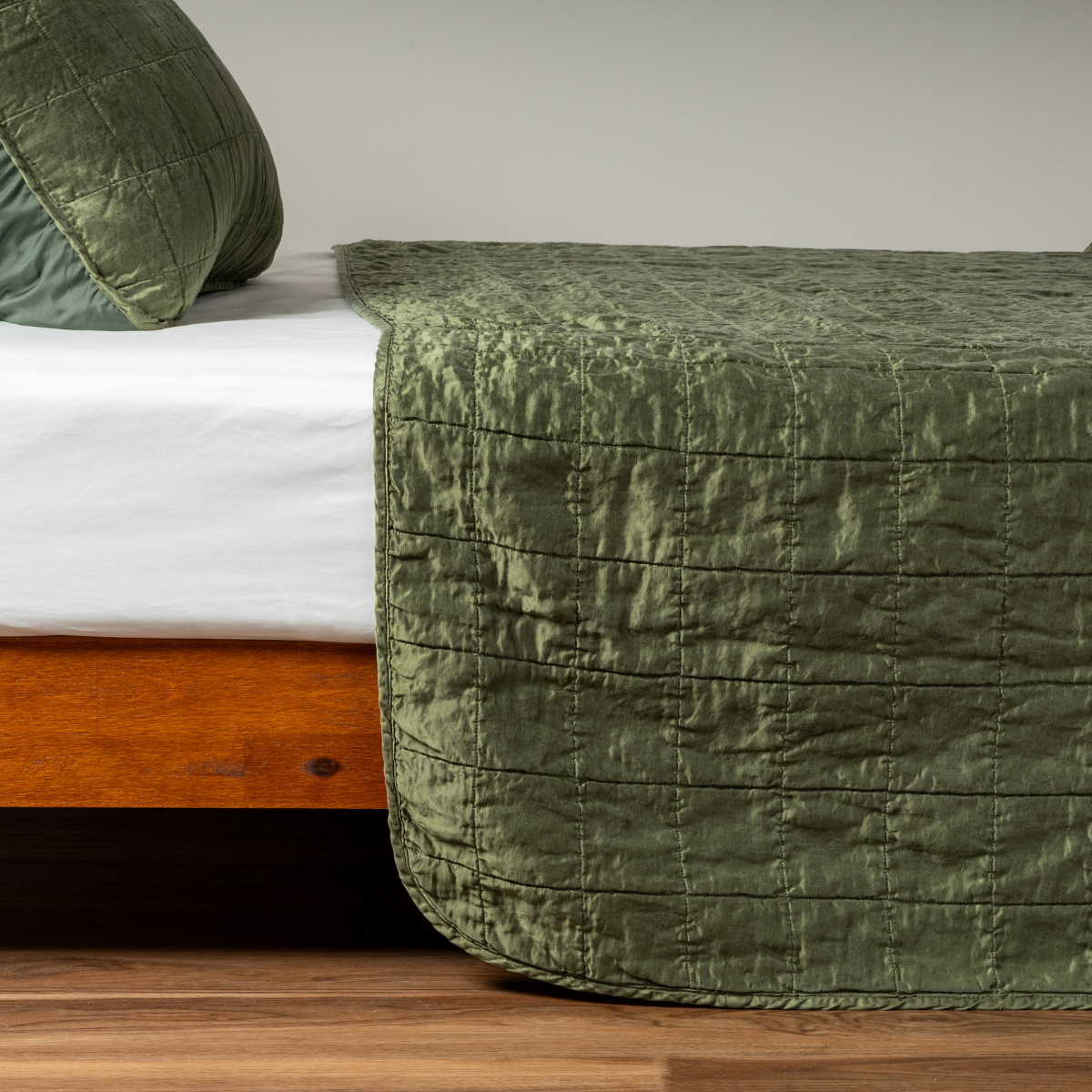 Sel Coverlet | Juniper | A side shot of a square quilted charmeuse coverlet in juniper, a deeply saturated dark green, with its matching sham.