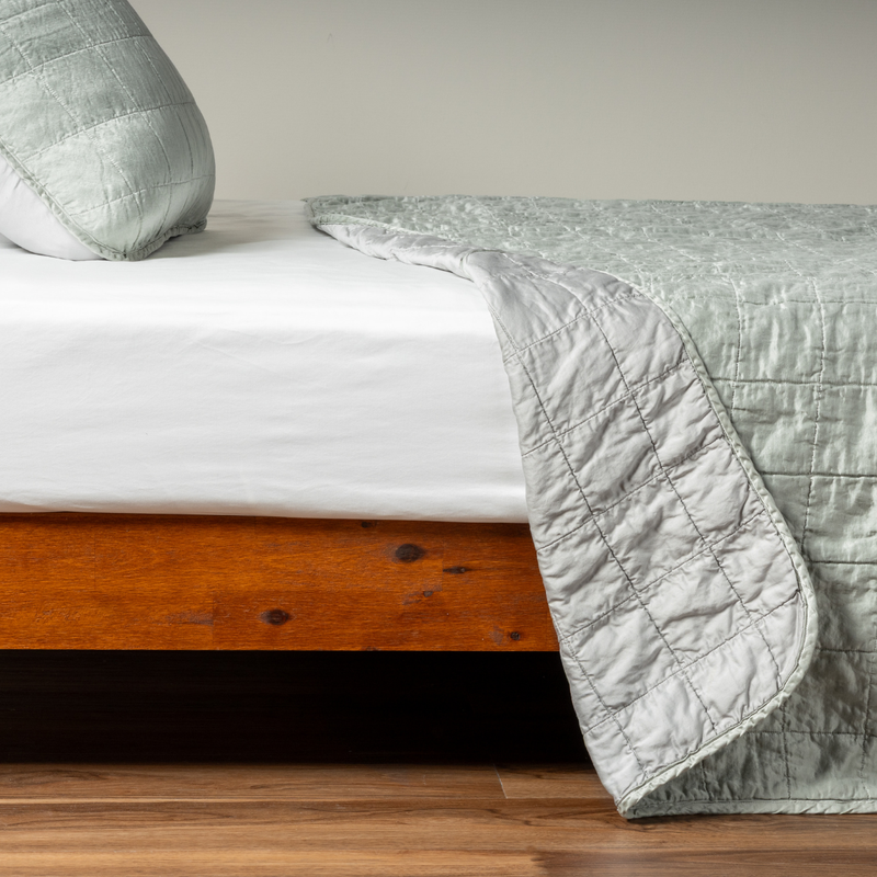 Sel Coverlet | Mineral | A side shot of a square quilted charmeuse coverlet in mineral, a soothing seafoam blue with subtle grey-green undertones, with its matching sham, the corner of the coverlet peeled back, revealing the cotton sateen back.