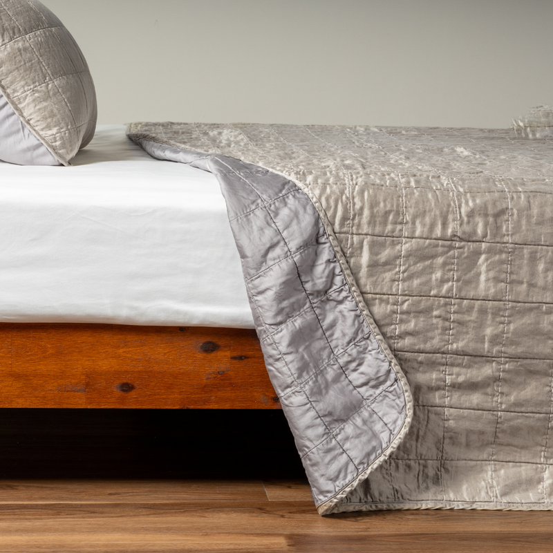 Sel Coverlet | Moonlight | A side shot of a square quilted charmeuse coverlet in moonlight, a saturated, cool, mid-dark grey tone, with its matching sham, the corner of the coverlet peeled back, revealing the cotton sateen back.