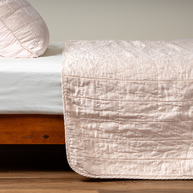 Sel Coverlet | Pearl | A side shot of a square quilted charmeuse coverlet in pearl, a soft rose pink tone, with its matching sham.