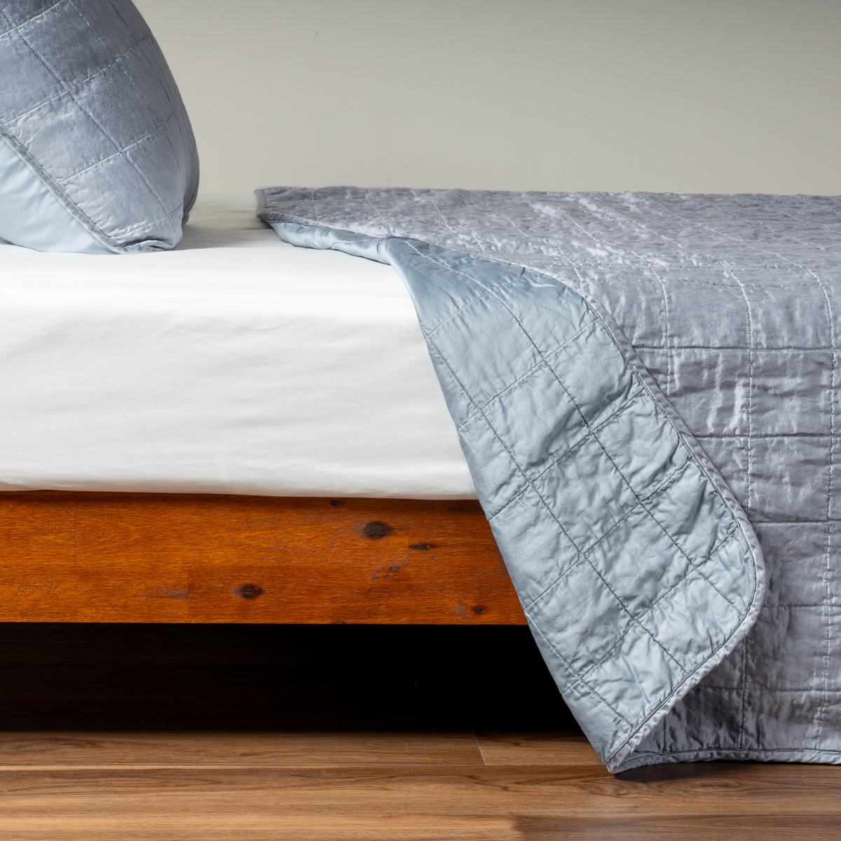 Sel Coverlet | Tahoe Blue | A side shot of a square quilted charmeuse coverlet in tahoe blue, a crisp true blue, with its matching sham, the corner of the coverlet peeled back, revealing the cotton sateen back.