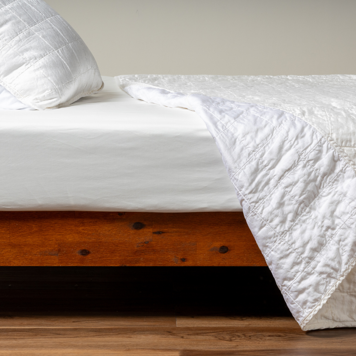 Sel Coverlet | White | A side shot of a square quilted charmeuse coverlet in white, with its matching sham, the corner of the coverlet peeled back, revealing the cotton sateen back.