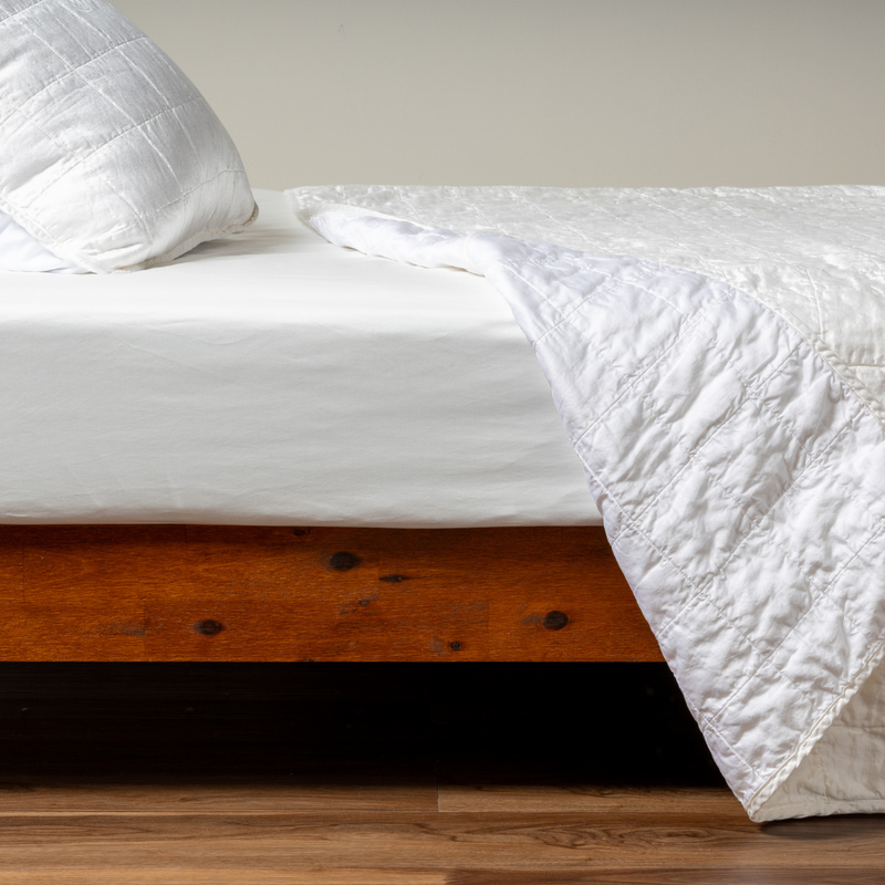 Sel Coverlet | White | A side shot of a square quilted charmeuse coverlet in white, with its matching sham, the corner of the coverlet peeled back, revealing the cotton sateen back.