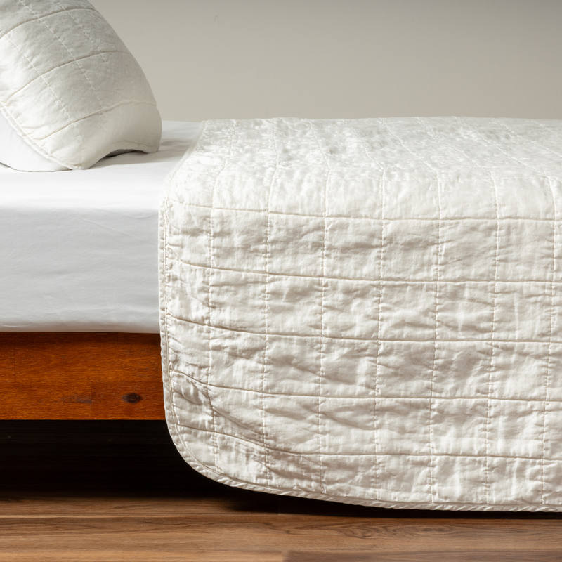 Sel Coverlet | Winter White | A side shot of a square quilted charmeuse coverlet in winter white, a softer and warmer tone than our classic white, with its matching sham.