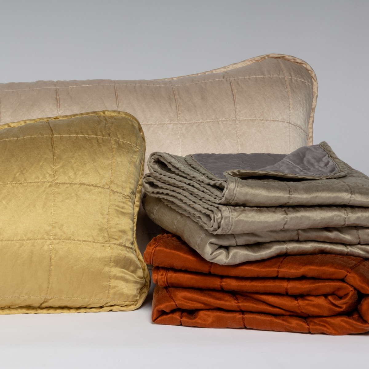 Sel Blanket | A cluster shot of square-quilted throw pillows and blankets shown against a white background.