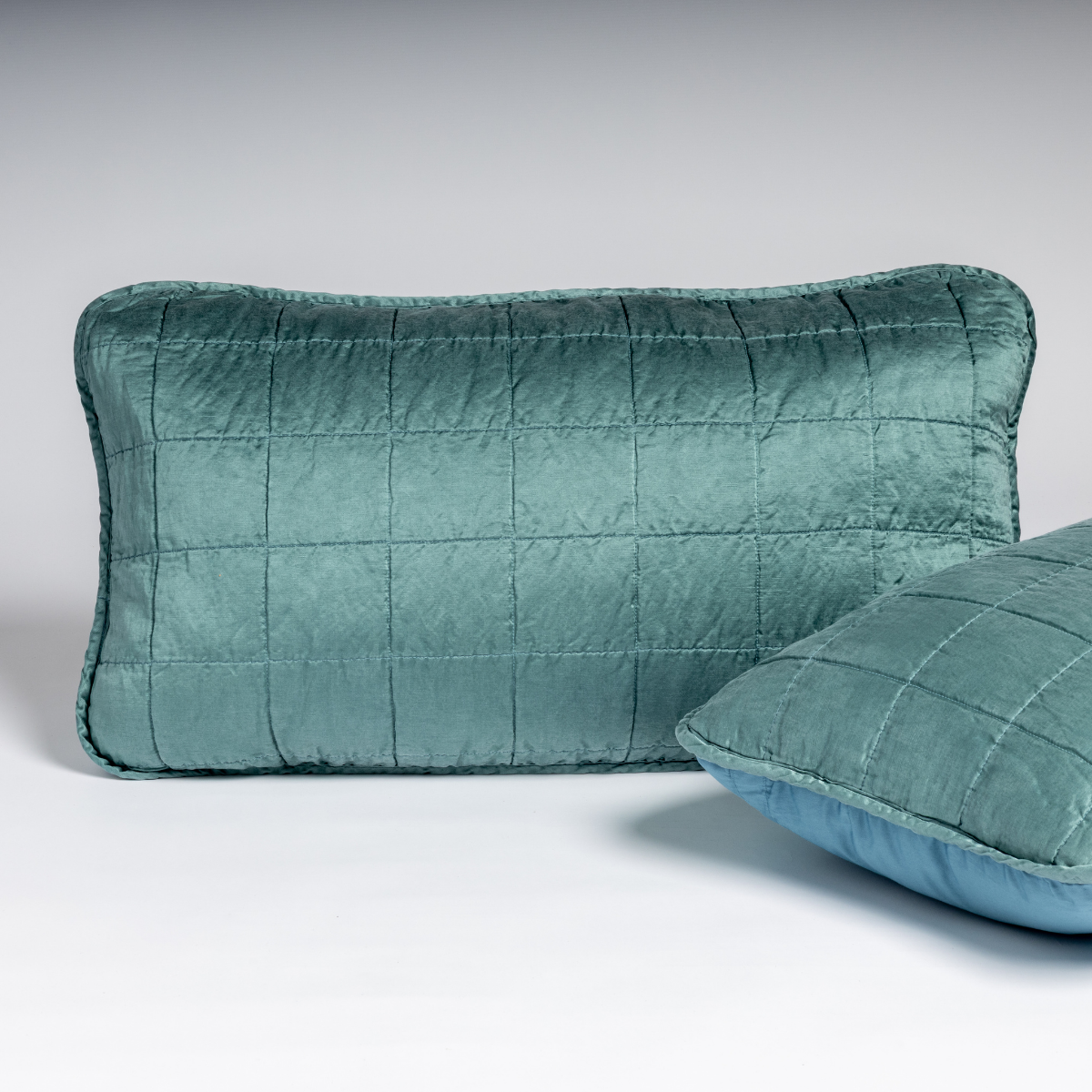 Sel Sham | Cenote | A pair of shams shown against a white background in cenote, a vibrant ocean-inspired blue-green, with one sham upright and the other on its side to show the cotton sateen back and square-quilted charmeuse front.