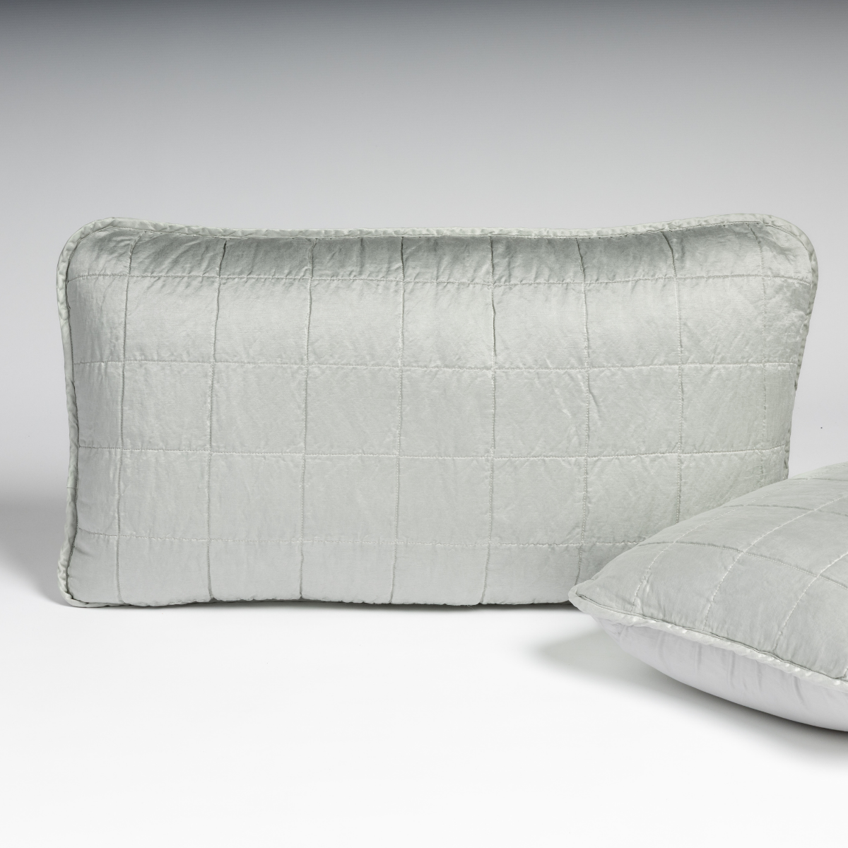 Sel Sham | Cloud | A pair of shams in cloud, a subtle sky blue-grey, shown against a white background with one sham upright and the other on its side to show the cotton sateen back and square-quilted charmeuse front.