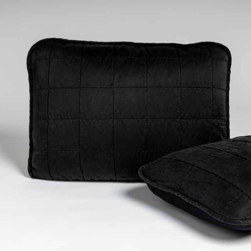 Sel Sham | Corvino | A pair of shams shown in corvino, our classic black, against a white background with one sham upright and the other on its side to show the cotton sateen back and square-quilted charmeuse front.