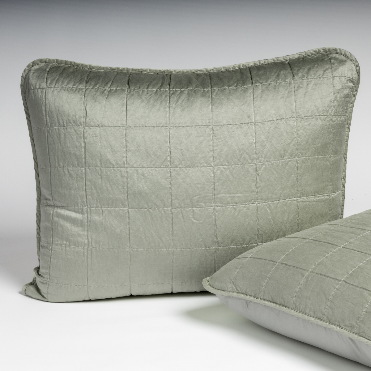 Sel Sham | Eucalyptus | A pair of shams in eucalyptus, a soft light green, shown against a white background with one sham upright and the other on its side to show the cotton sateen back and square-quilted charmeuse front.