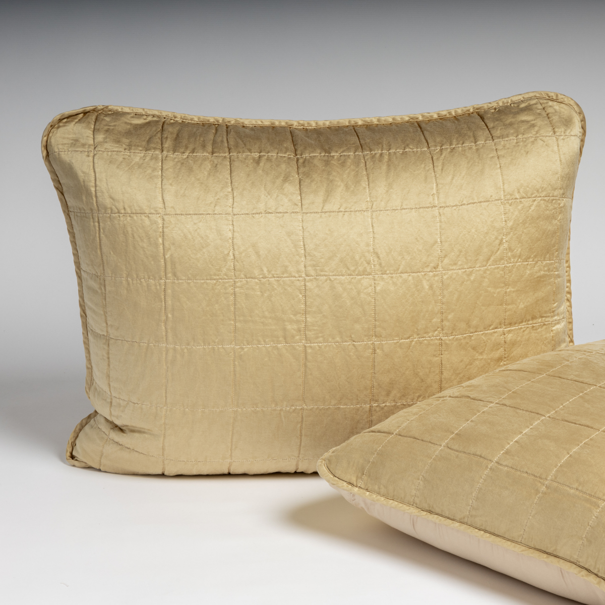 Sel Sham | Honeycomb | A pair of shams in honeycomb, a warm golden tone, shown against a white background with one sham upright and the other on its side to show the cotton sateen back and square-quilted charmeuse front.