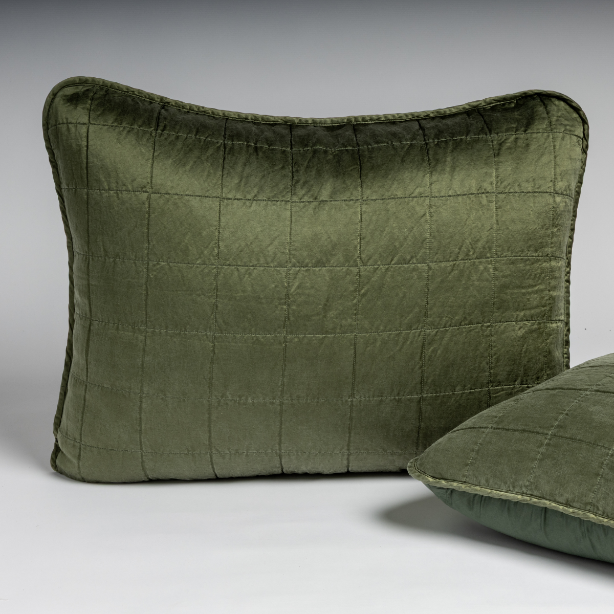 Sel Sham | Juniper | A pair of shams in juniper, a deeply saturated dark green, shown against a white background with one sham upright and the other on its side to show the cotton sateen back and square-quilted charmeuse front.