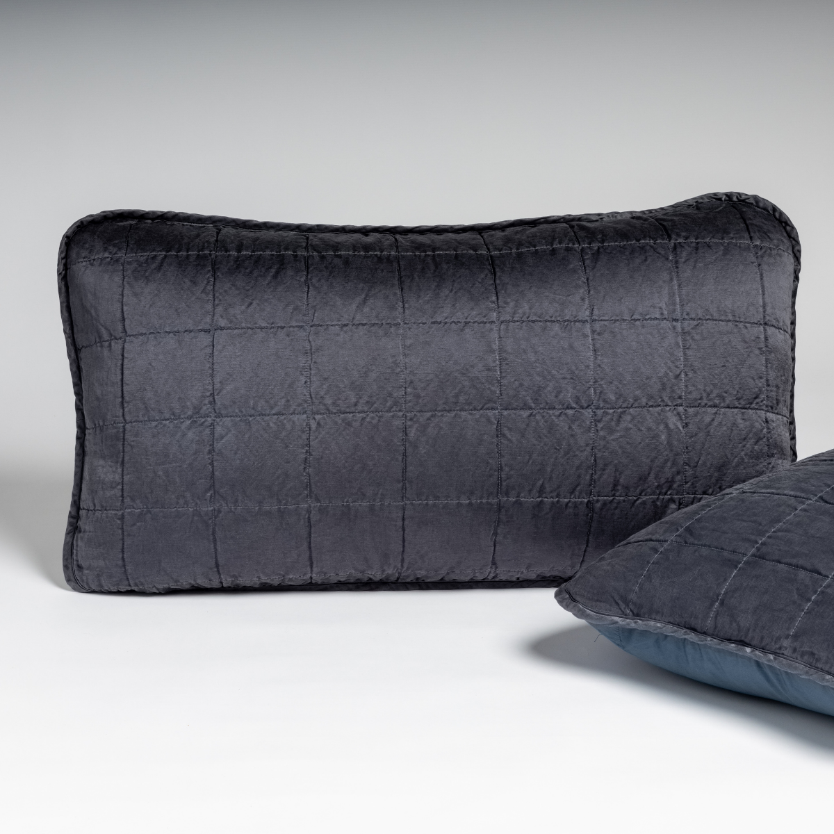 Sel Sham | Midnight | A pair of shams in midnight, a rich indigo tone, shown against a white background with one sham upright and the other on its side to show the cotton sateen back and square-quilted charmeuse front.