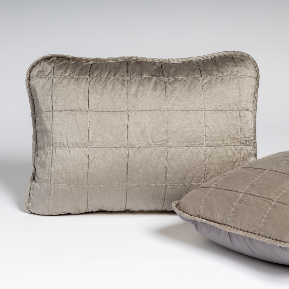 Sel Sham | Moonlight | A pair of shams in moonlight, a saturated, cool, mid-dark grey tone, shown against a white background with one sham upright and the other on its side to show the cotton sateen back and square-quilted charmeuse front.