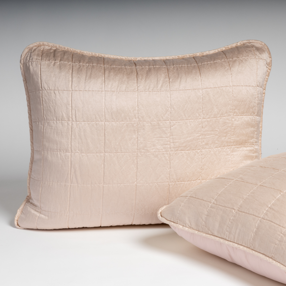Sel Sham | Pearl | A pair of shams in pearl, a soft rose pink tone, shown against a white background with one sham upright and the other on its side to show the cotton sateen back and square-quilted charmeuse front.