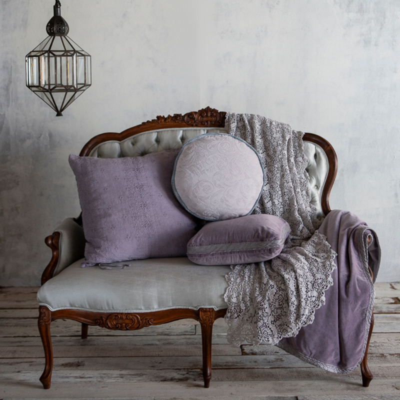 Allora Bed Scarf | lace bed scarf draped on a parlor sofa with an assortment of throw pillows and a cotton velvet throw blanket.