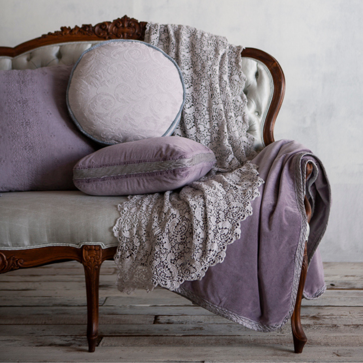 An antique sofa piled with throw pillows and blankets in french lavender and cloud