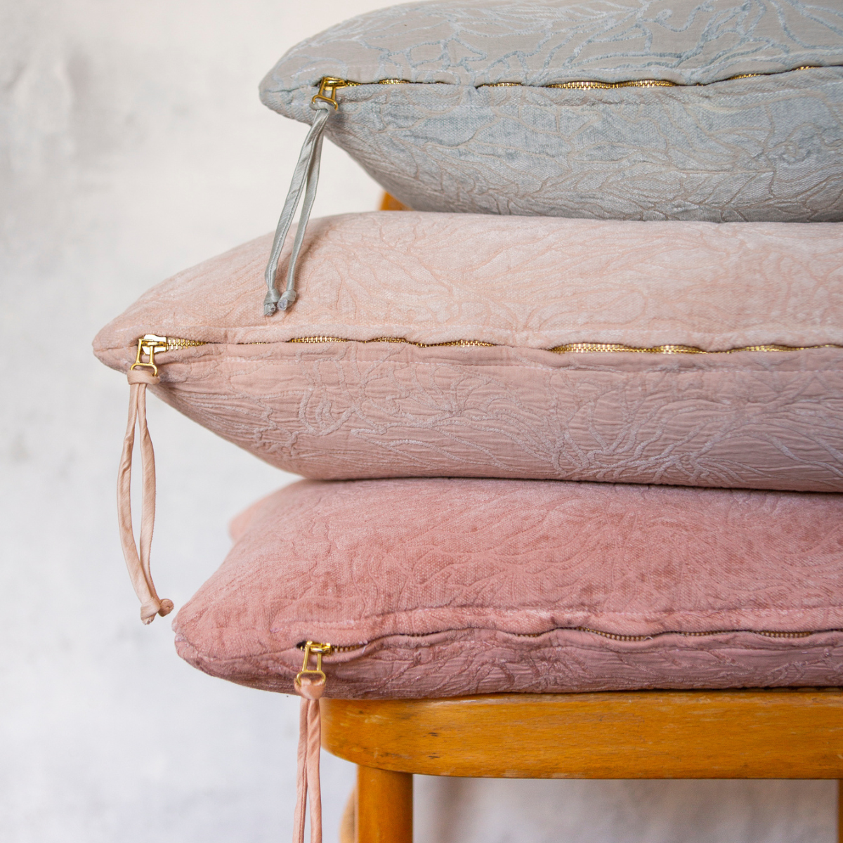 Georgia Throw Pillow | light and warm colored throw pillows in cotton and chenille jacquard shown stacked against a light grey wall, somewhat closeup with the bottom zippers and pulls visible in the shot.