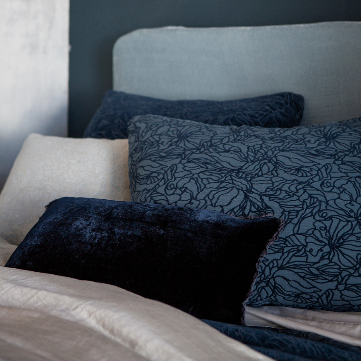 Georgia Sham | shams and a throw pillow shown against a light blue headboard all in blue tones.