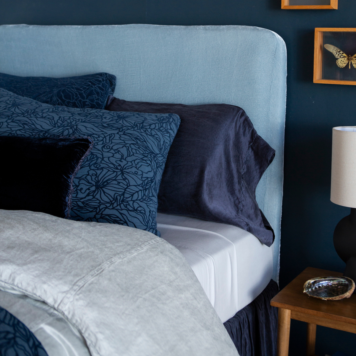 Georgia Sham | midnight colored sleeping pillow, shams and throw pillow shown against a light blue headboard on a dark blue wall. The sheets are perfectly tucked and the duvet cover is intentionally folded back to show the pillow arrangement