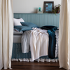 Georgia Bedspread | side view of a bed dressed with lace pillowcases, flat sheet, bed skirt and bed scarf layered with cotton sateen sheets, chenille and cotton jacquard bedspread and shams and silk velvet accent pillow and bed end blanket — shown from the side with curtain panels framing the bed that's against a light blue paneled wall.