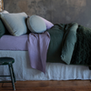 Harlow Throw Pillow | Eucalyptus | cotton velvet round pillow and sham shown with linen and cotton velvet bedding in green and purple tones - side view of the bed.