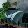 Juniper | a linen duvet cover cover with linen sheets in eucalyptus and pillows and coverlet and throw blanket all in juniper - a twin bed shown into the corner with several live plants and black rug on a wooden floor.