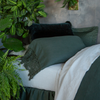 Linen Fitted Sheet | a close up of the head of a twin bed dressed in linen sheets with sham, throw pillows and sleeping pillow arranged among live plants.