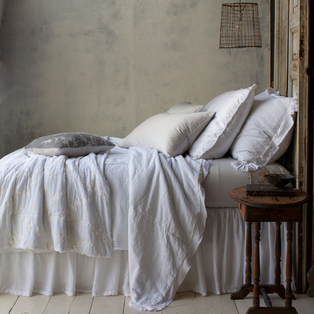 Bria Twin Fitted Sheets | Sterling Bria sheets contrast against a mostly white bed, shown from the side. The lighting is moody and colors are muted, emphasizing the variety of cotton, linen, and silk textures.