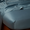 Bria Twin Flat Sheet | Cenote | Cotton sateen flat sheet draped over matching fitted sheet. Shown from the top corner, the flat sheet is rumpled, highlighting the shine of the fabric.