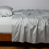 Bria Twin Flat Sheet | Cloud | Cotton sateen flat sheet, shown with matching fitted sheet and sleeping pillow - side view.