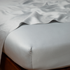 Bria Twin Flat Sheet | Cloud | Cotton sateen flat sheet draped over matching fitted sheet. Shown from the top corner, the flat sheet is rumpled, highlighting the shine of the fabric.