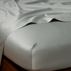 Bria Twin Flat Sheet | Eucalyptus | Cotton sateen flat sheet draped over matching fitted sheet. Shown from the top corner, the flat sheet is rumpled, highlighting the shine of the fabric.