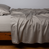 Bria Twin Flat Sheet | Fog | Cotton sateen flat sheet, shown with matching fitted sheet and sleeping pillow - side view.