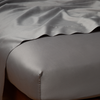 Bria Twin Flat Sheet | Moonlight | Cotton sateen flat sheet draped over matching fitted sheet. Shown from the top corner, the flat sheet is rumpled, highlighting the shine of the fabric.