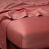 Bria Twin Flat Sheet | Poppy | Cotton sateen flat sheet draped over matching fitted sheet. Shown from the top corner, the flat sheet is rumpled, highlighting the shine of the fabric.