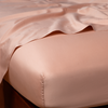 Bria Twin Flat Sheet | Rouge | Cotton sateen flat sheet draped over matching fitted sheet. Shown from the top corner, the flat sheet is rumpled, highlighting the shine of the fabric.