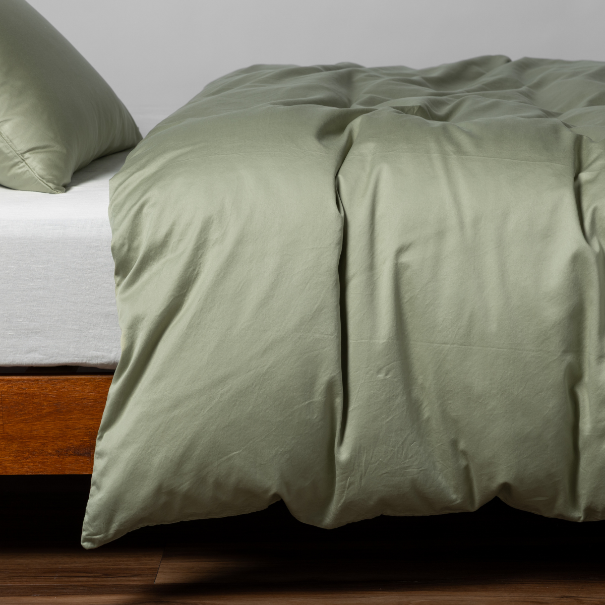 Desert Sage | matching bria duvet cover and pillowcase in desert sage, a serenely elegant green, offering a hushed hue, shown from the side on a bed against a plain background.