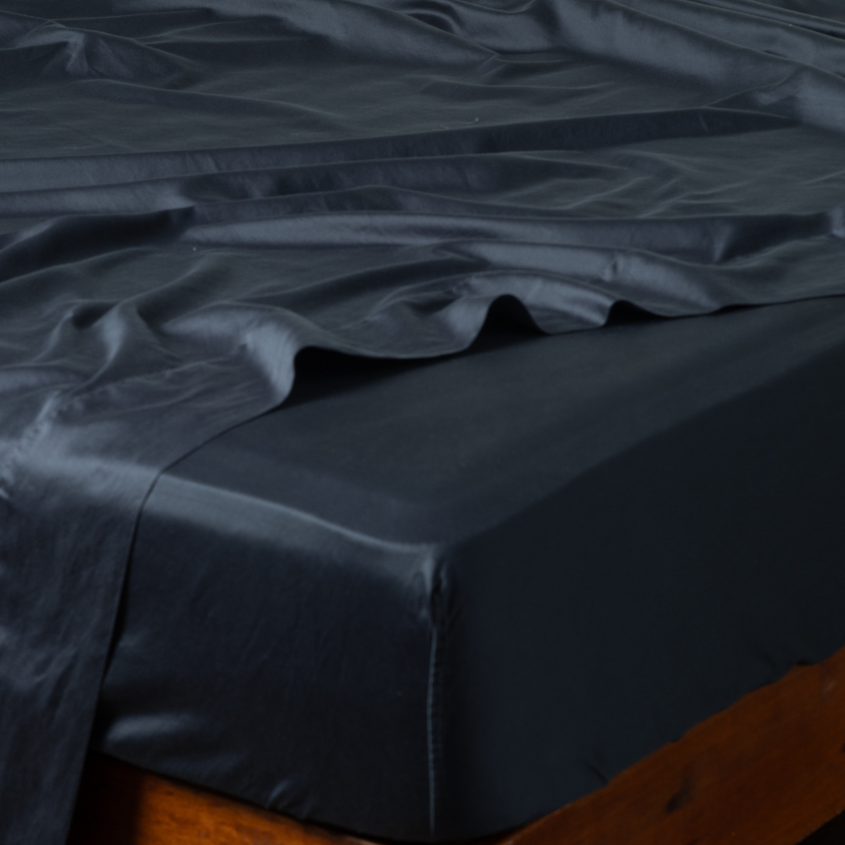 Bria Twin Fitted Sheets | Slate | ccotton sateen fitted sheet on a mattress with its matching flat sheet shown from the corner on a wooden bedframe.