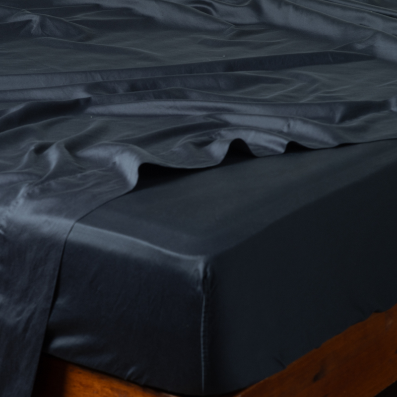 Bria Twin Fitted Sheets | Slate | ccotton sateen fitted sheet on a mattress with its matching flat sheet shown from the corner on a wooden bedframe.
