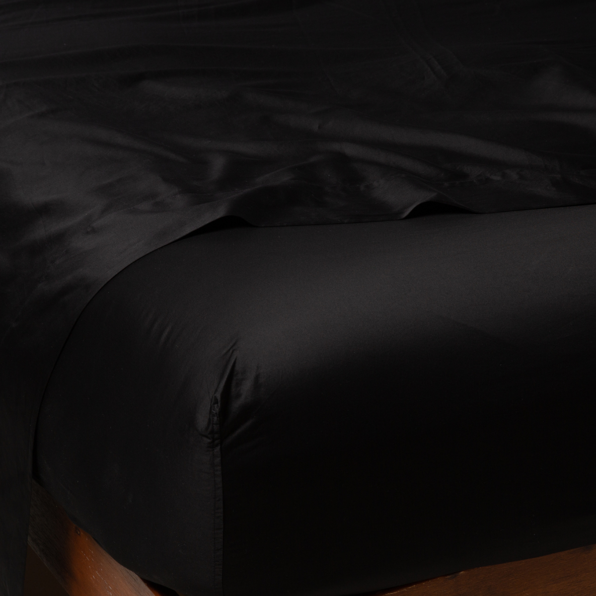 Bria Twin Flat Sheet | Corvino | Cotton sateen flat sheet draped over matching fitted sheet. Shown from the top corner, the flat sheet is rumpled, highlighting the shine of the fabric.