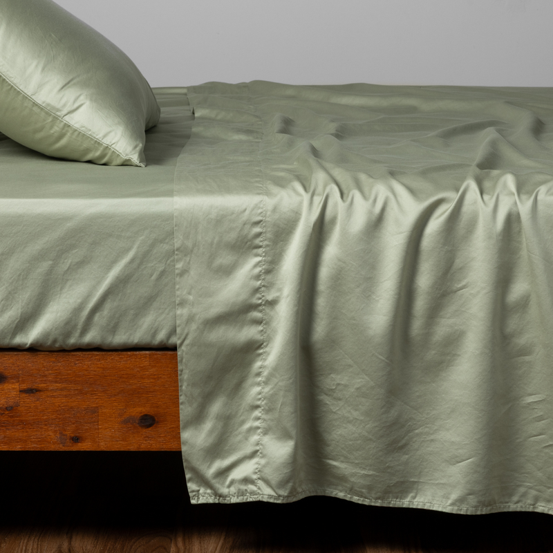 Bria Twin Flat Sheet | Desert Sage | a matching flat sheet, fitted sheet and  pillowcase in desert sage, a serenely elegant green, offering a hushed hue, shown from the side angle on a bed.