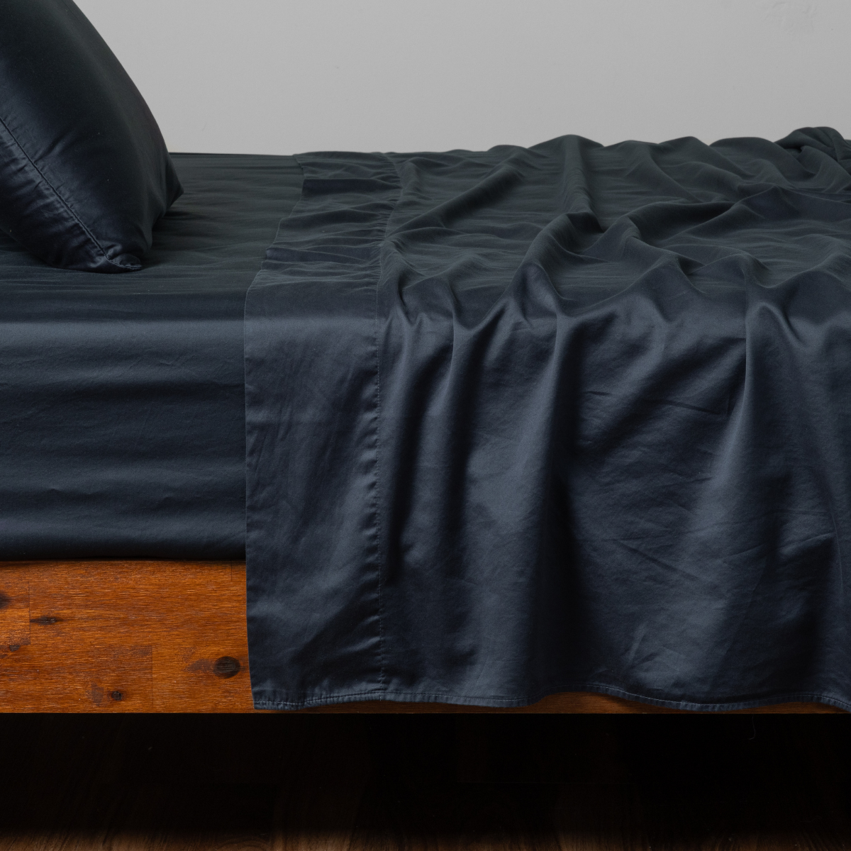 Bria Twin Flat Sheet | Slate | cotton sateen sheets with matching pillowcase shown from the side on a bed against a white background.