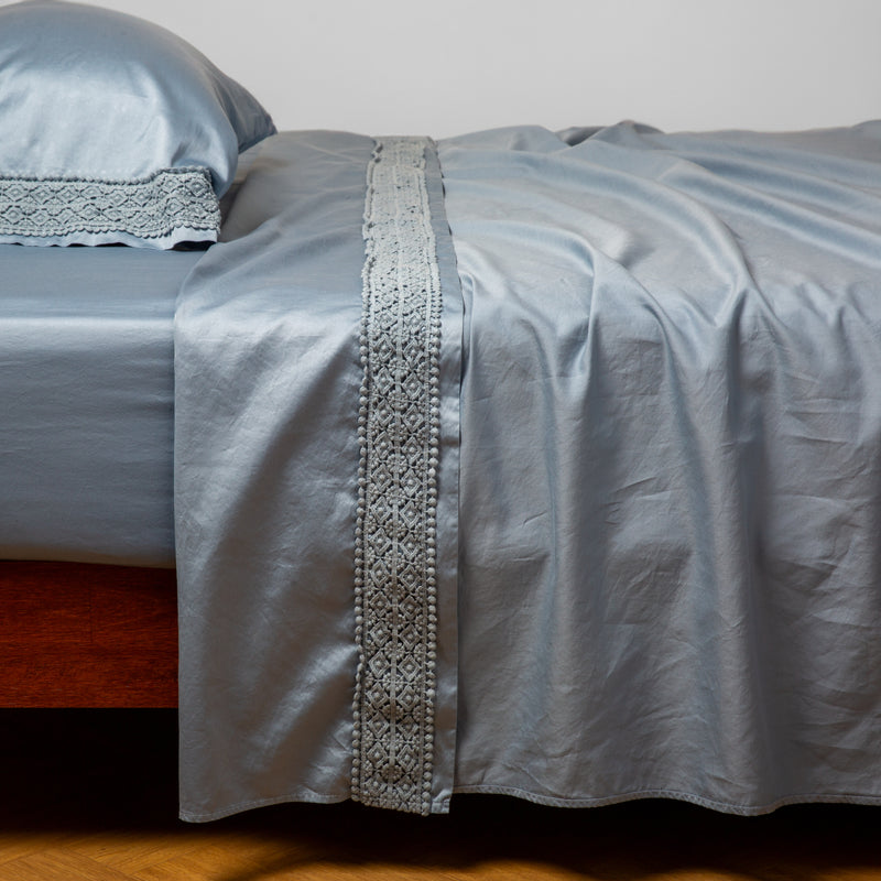 Bria Pillowcase (Single) | Tahoe Blue | Cotton sateen sleeping pillow and flat sheet embellished with cotton lace trim on a bed - side view.