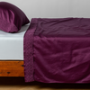 Bria Flat Sheet | Fig | Cotton sateen sleeping pillow and flat sheet embellished with cotton lace trim on a bed - side view.